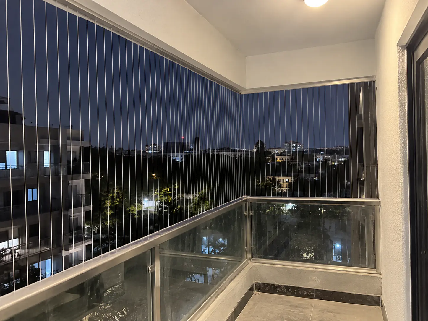 Invisible grill cables across a high-rise apartment balcony at night